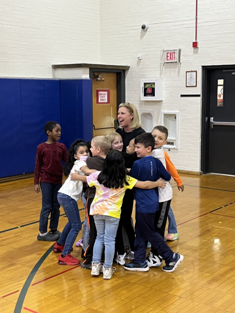 Kids hugging Mrs. Convey on the basketball court